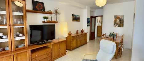 Una sala de estar con televisor, muebles de madera, un comedor con mesa y sillas, y obras de arte en las paredes.
