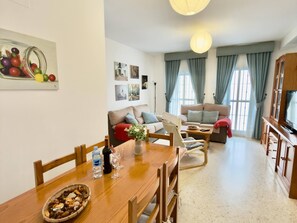 Ein Wohnzimmer mit Sofa, einem Esstisch mit Stühlen, einem Fernseher und einer Küchenzeile mit Schränken.