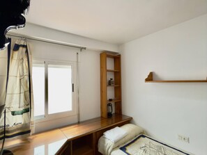 Une chambre à coucher avec un lit, une étagère en bois, une fenêtre avec des rideaux et une table de chevet.