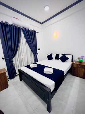 A hotel room with a bed, curtains, a bedside table, a nightstand, and a wall-mounted light. - Nilaveli Royal Paradise (Nilaveli)