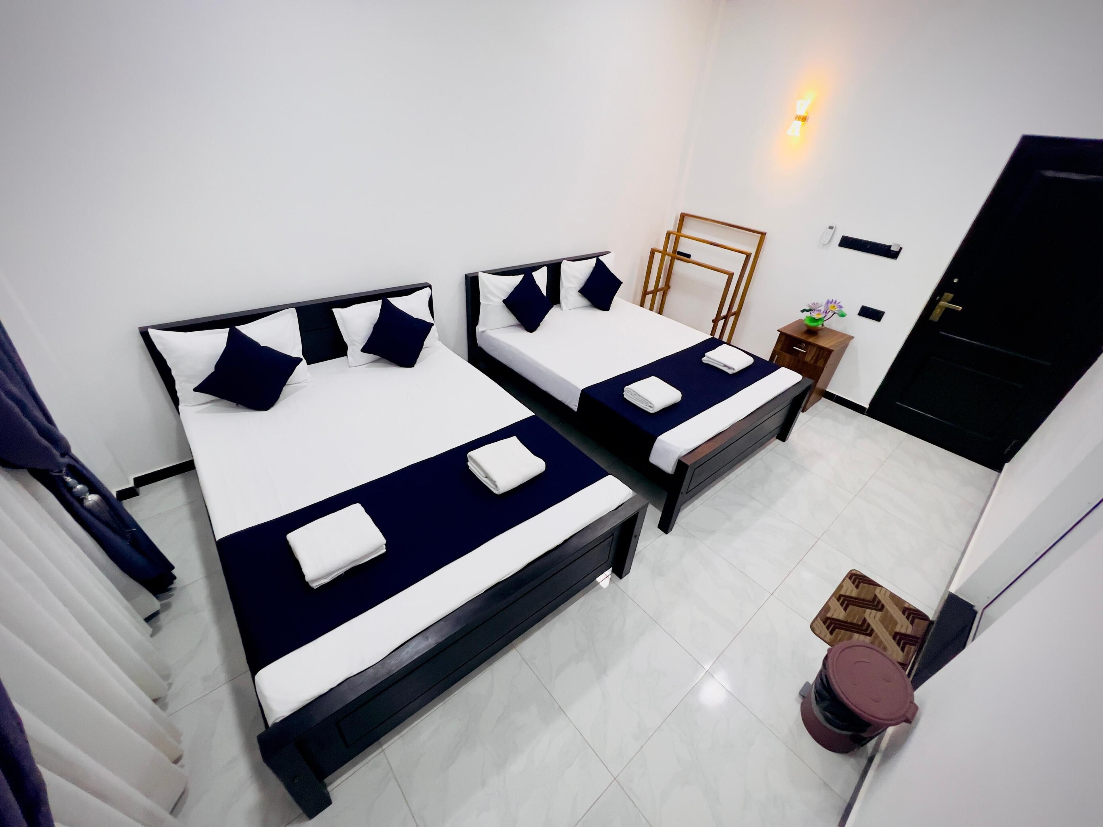 A hotel room with two beds, a small table with a plant, a door, and a wall-mounted light fixture.