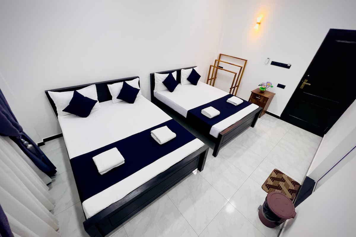 Habitación de hotel con dos camas, una mesita con una planta, una puerta y un aplique de pared.