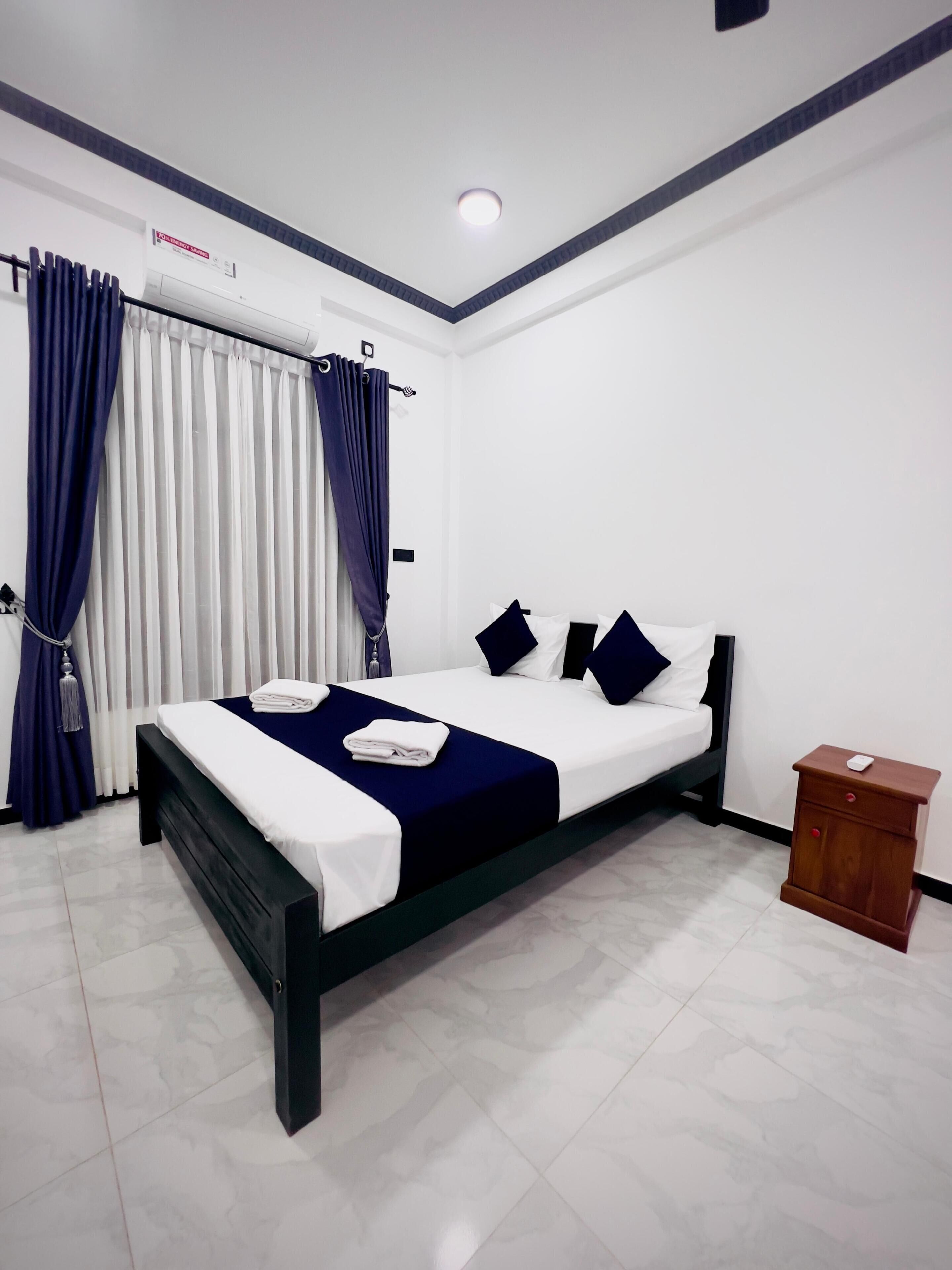 Una habitación de hotel moderna con cama, cortinas, unidad de aire acondicionado y una mesita de noche de madera.