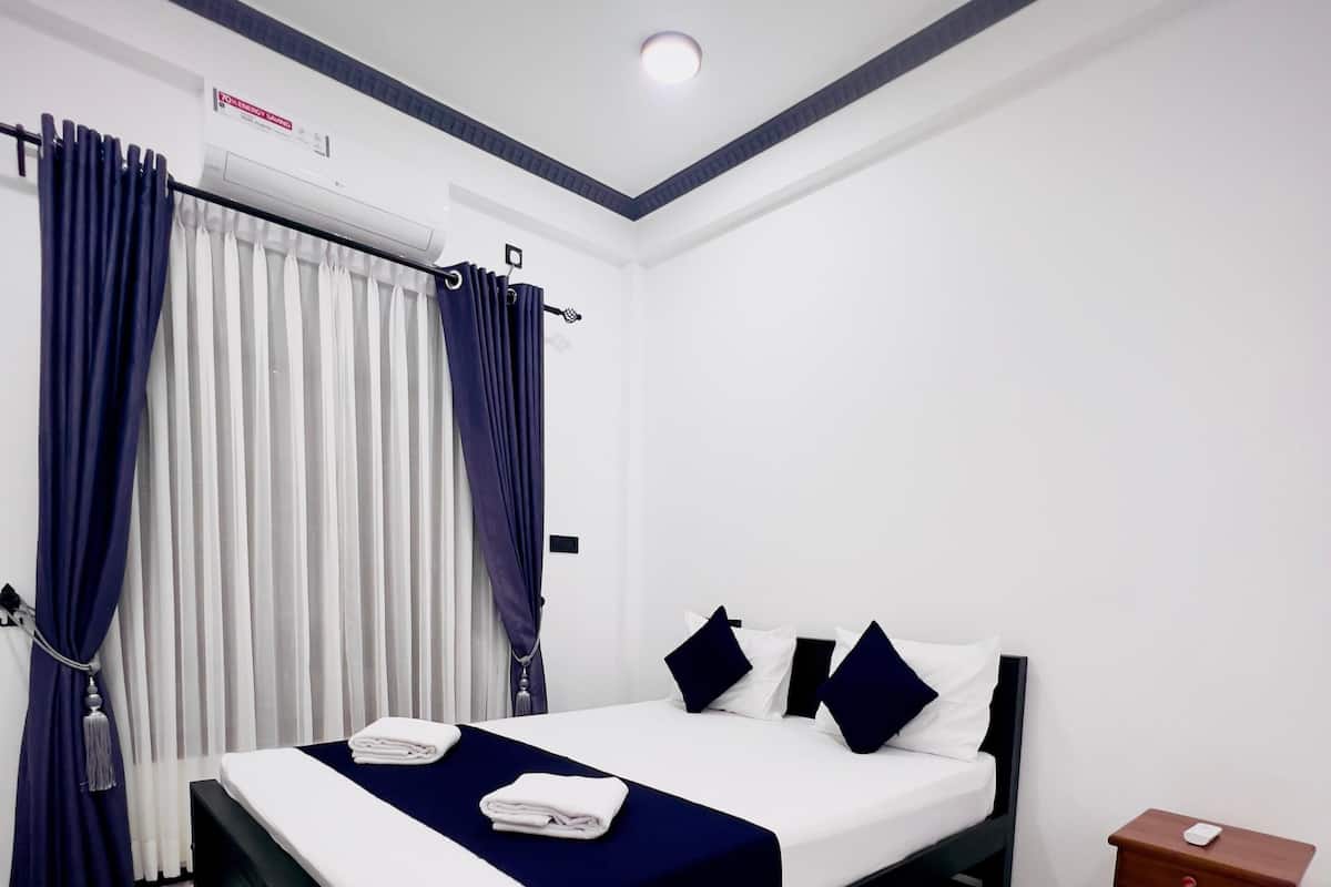 Quarto de hotel moderno com uma cama, cortinas, ar condicionado e uma pequena mesa de cabeceira de madeira.