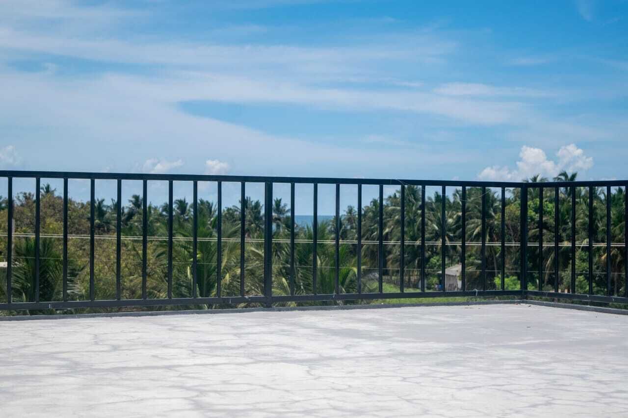 Un balcon doté d’une rambarde en métal, d’un sol en béton et offrant une vue sur les palmiers et l’océan.
