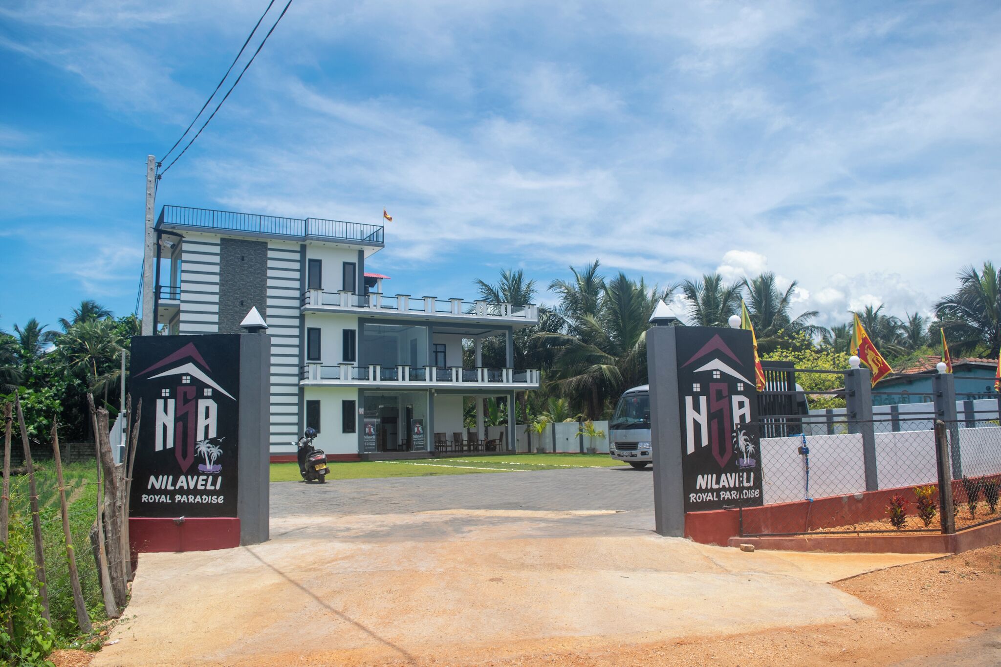 A modern building with a balcony, a sign reading 'NILAVELI ROYAL PARADISE,' and a fenced entrance.