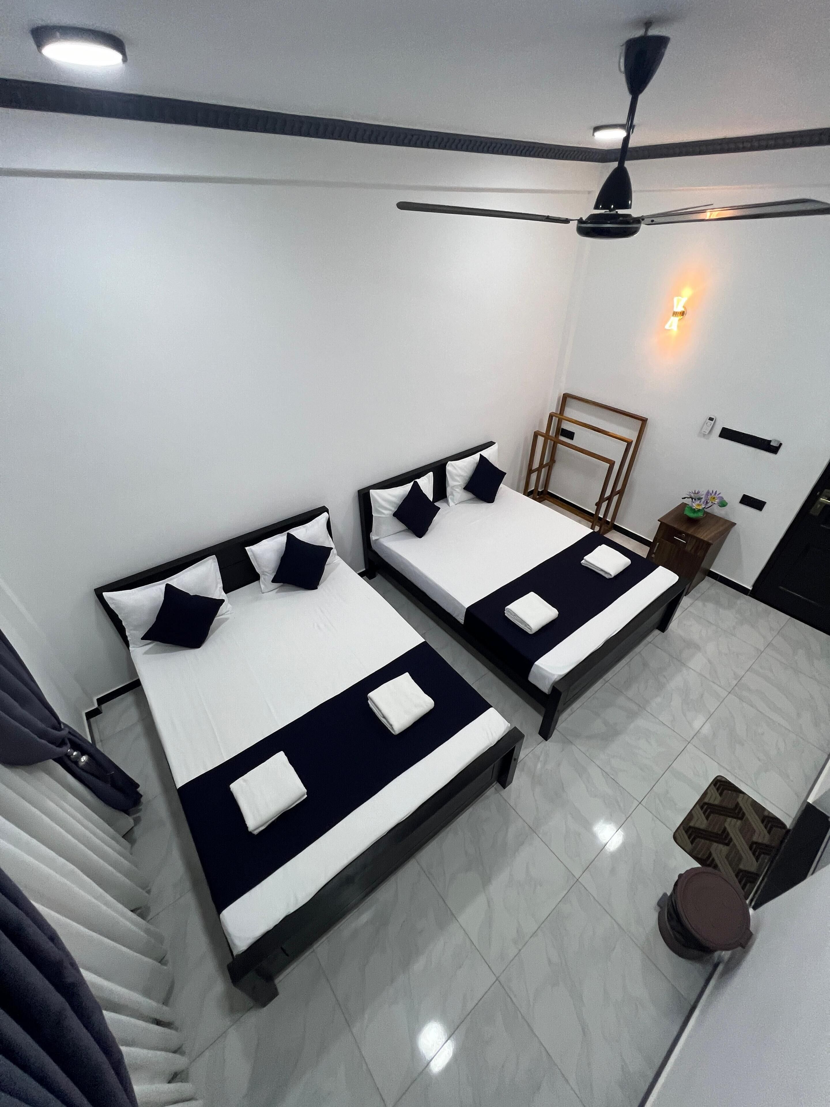Una habitación de hotel moderna con dos camas, un ventilador de techo, una mesita con una planta y una lámpara fijada a la pared.