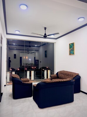 A modern living room with a sofa set, ceiling fan, recessed lighting, and a glass partition. - Nilaveli Royal Paradise (Nilaveli)