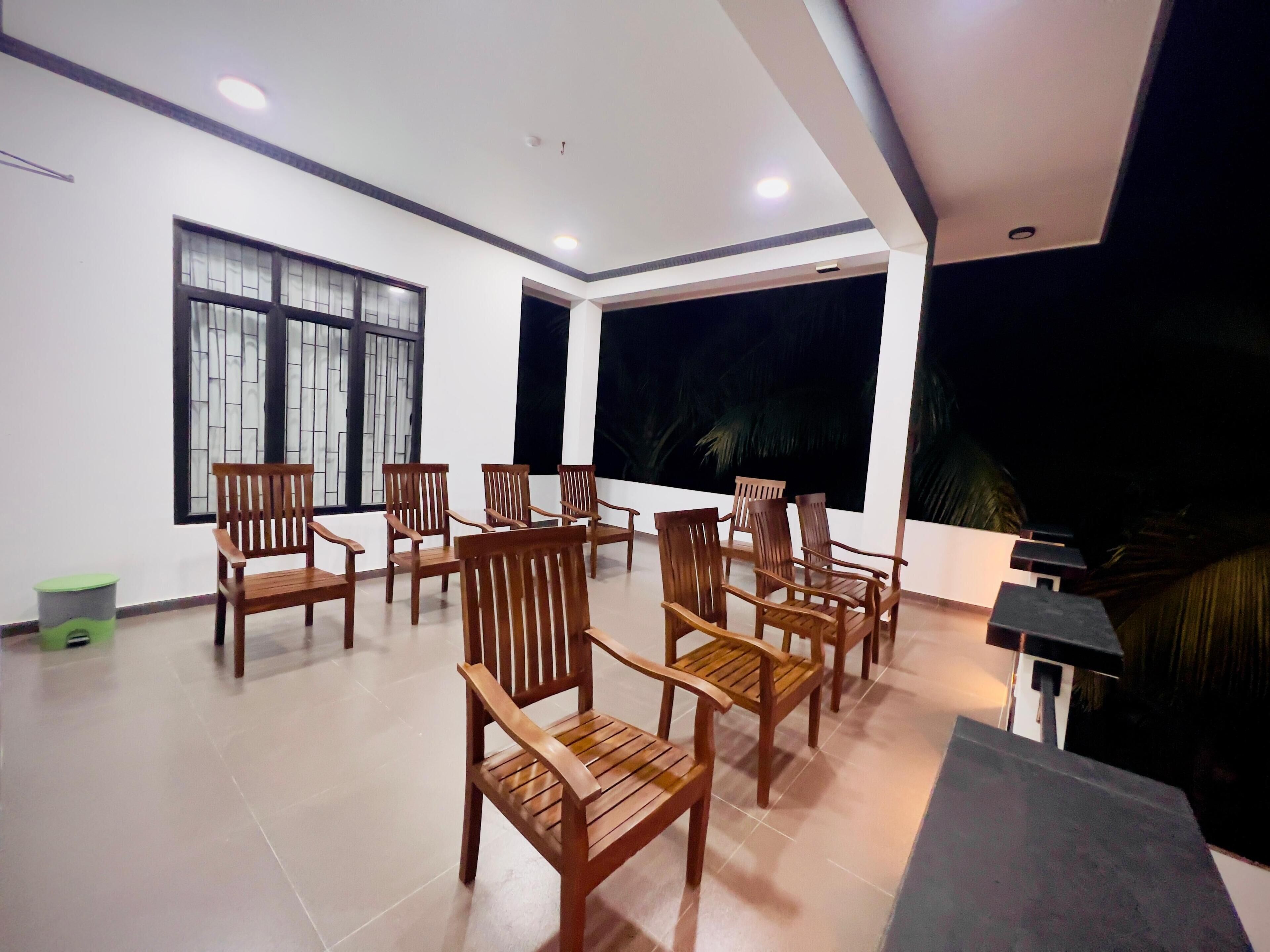 A room with multiple wooden chairs arranged in a semi-circle, large windows with dark curtains, and a ceiling with recessed lighting.