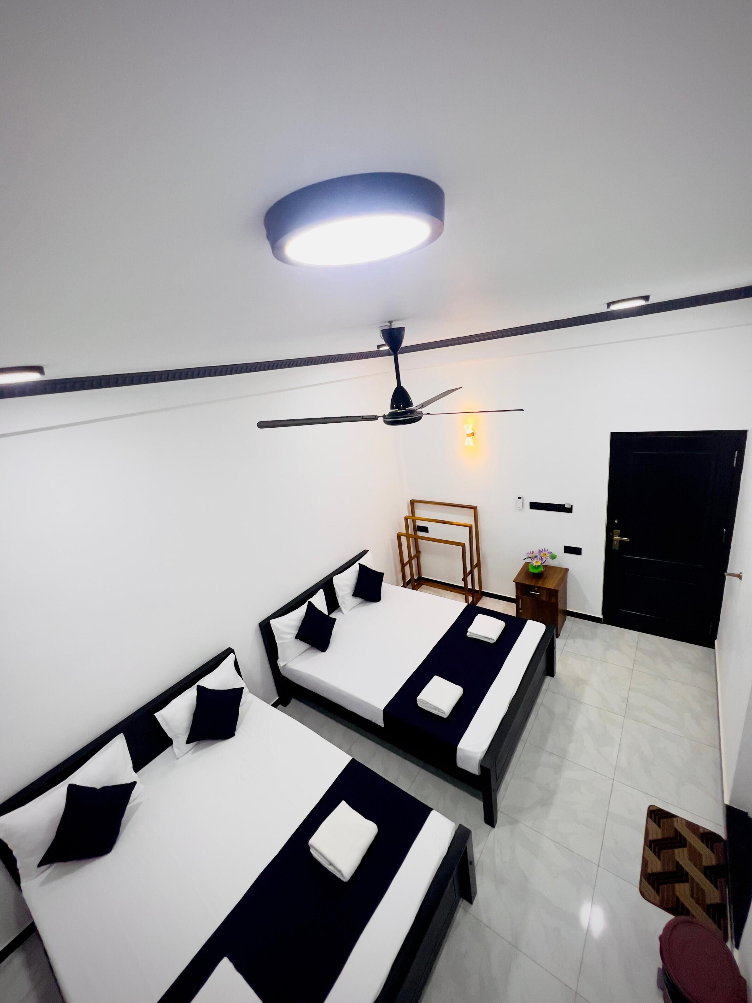 Una habitación con tres camas, un ventilador de techo, una mesita con una planta y una puerta.