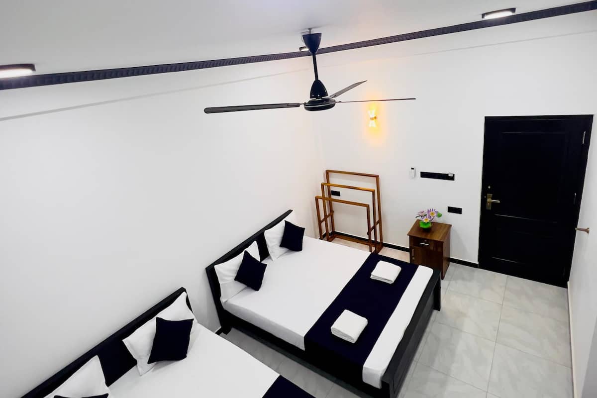 Quarto com três camas, um ventilador de teto, uma mesinha com uma planta e uma porta.