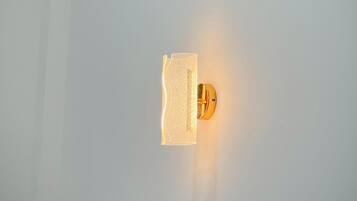 A wall-mounted light fixture with a textured glass panel and a gold-colored base.