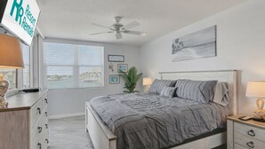 A bedroom with a bed, nightstands, a ceiling fan, a window with blinds, and a sign for Resort Rentals. - Bahia Del Mar 7-404 - Point Paradise (St. Petersburg)