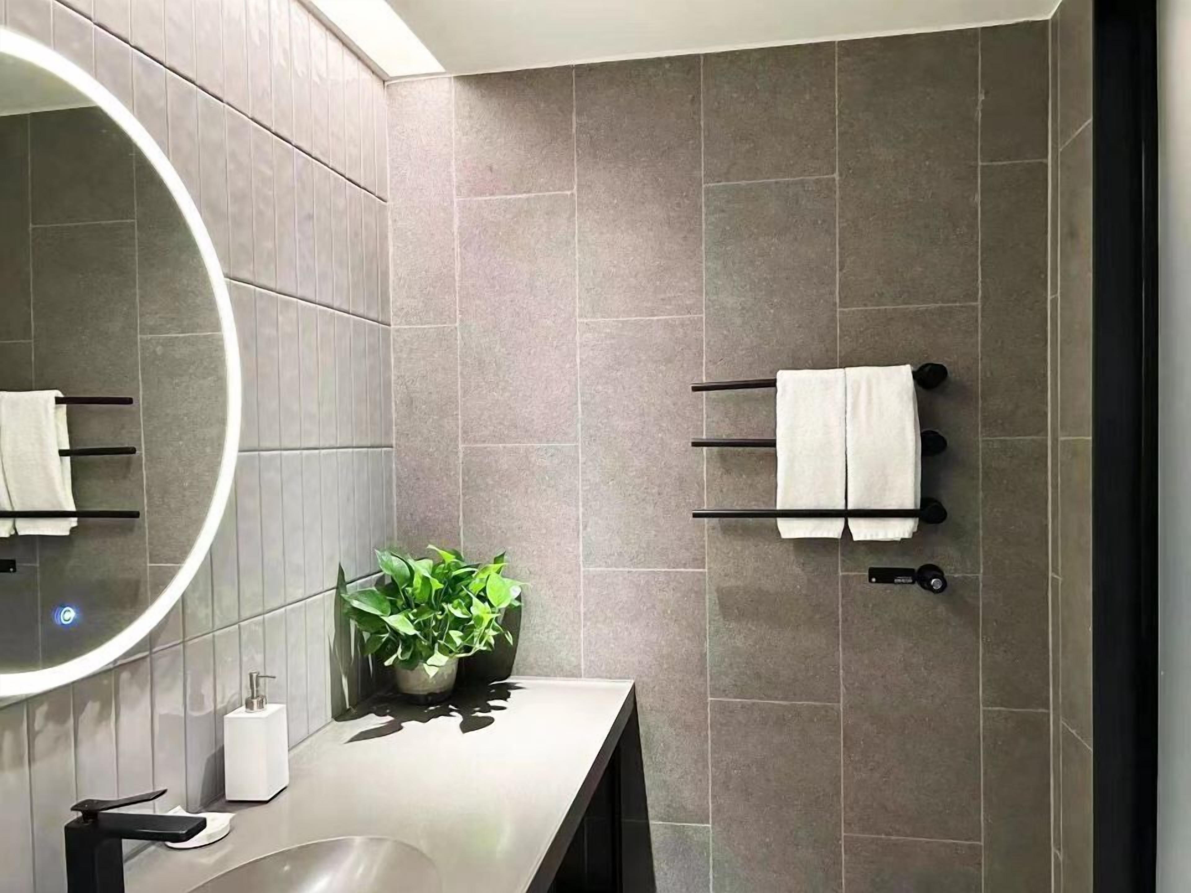 Ein modernes Badezimmer mit rundem Spiegel, Waschbecken, einer Topfpflanze und Handtuchhaltern.