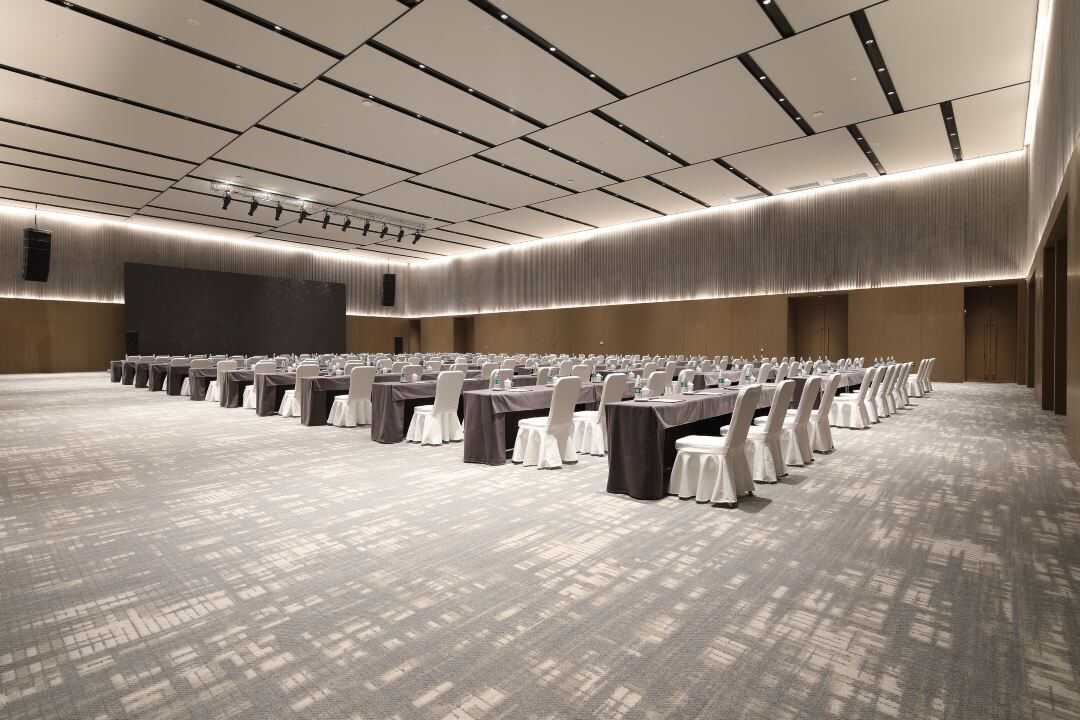 A large conference room with rows of tables and chairs, a large screen, and a patterned carpet.