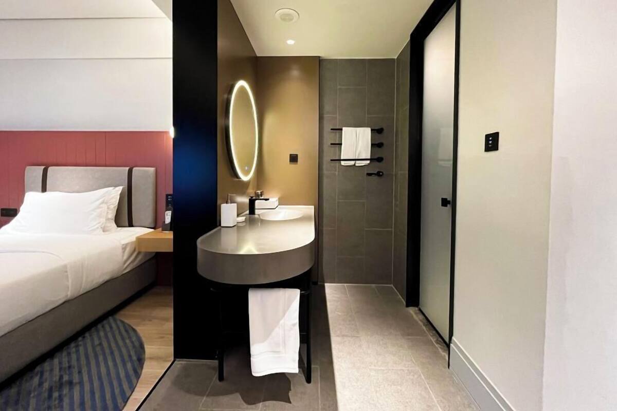 Ein modernes Hotelzimmer mit einem Bett, einem runden Waschtisch und einer separaten Dusche.