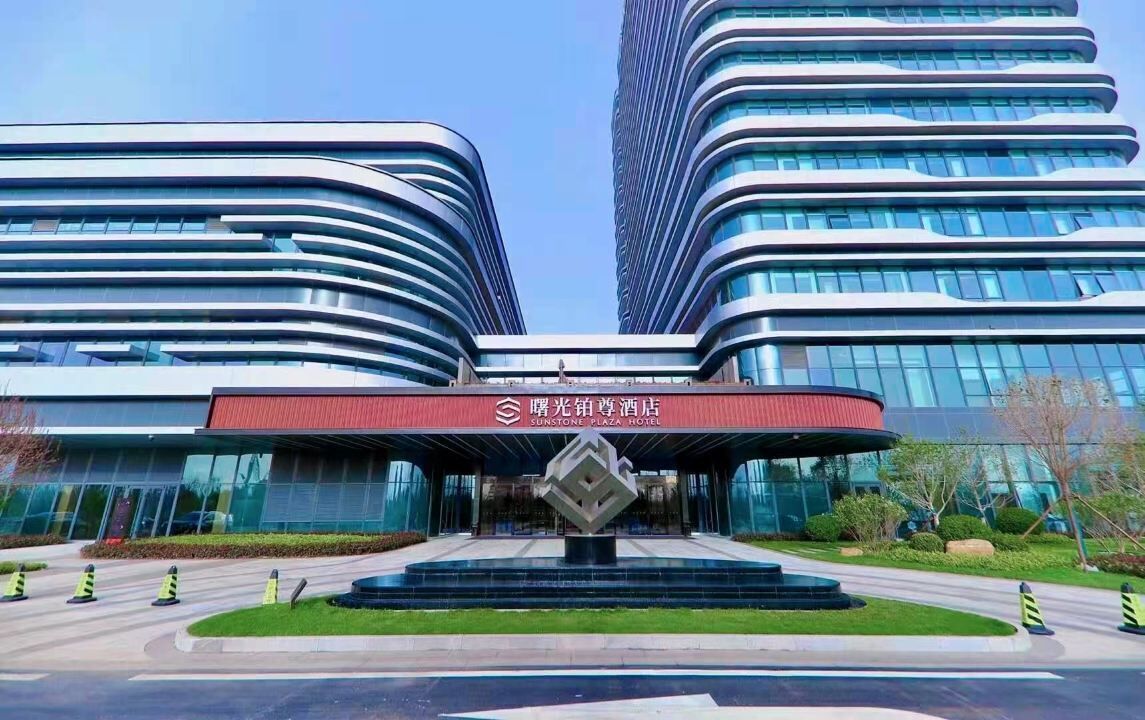 Un hotel moderno con una fachada curva distintiva y una entrada central que presenta una gran escultura geométrica.