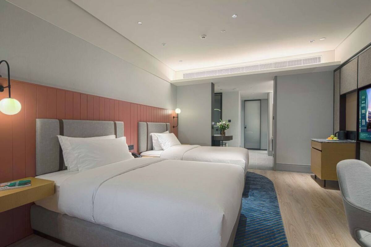 Ein Hotelzimmer mit zwei Betten, einem Schreibtisch, einem Stuhl und einem Fernseher.