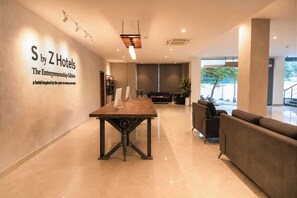 Un hall de hotel con mostrador de recepción, zona de estar y un letrero en la pared.