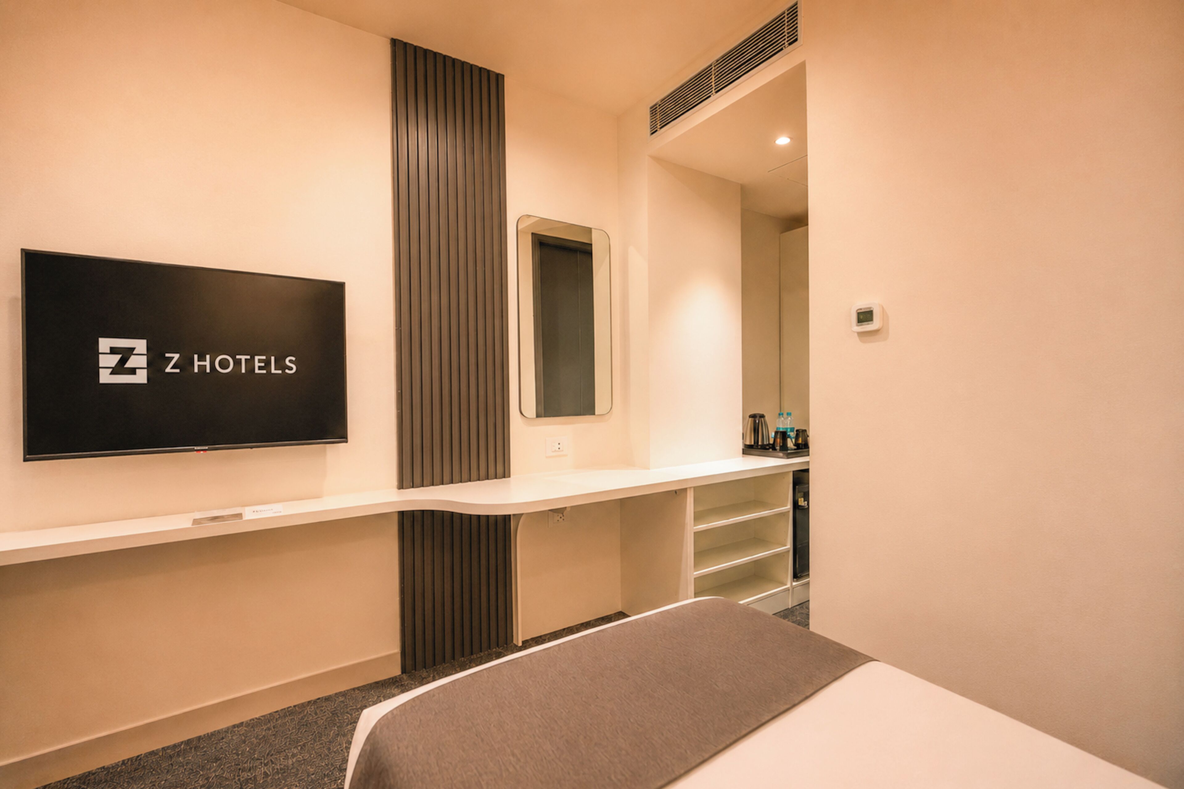 A hotel room with a flat-screen TV, a mirror, a bedside table, and a bed.