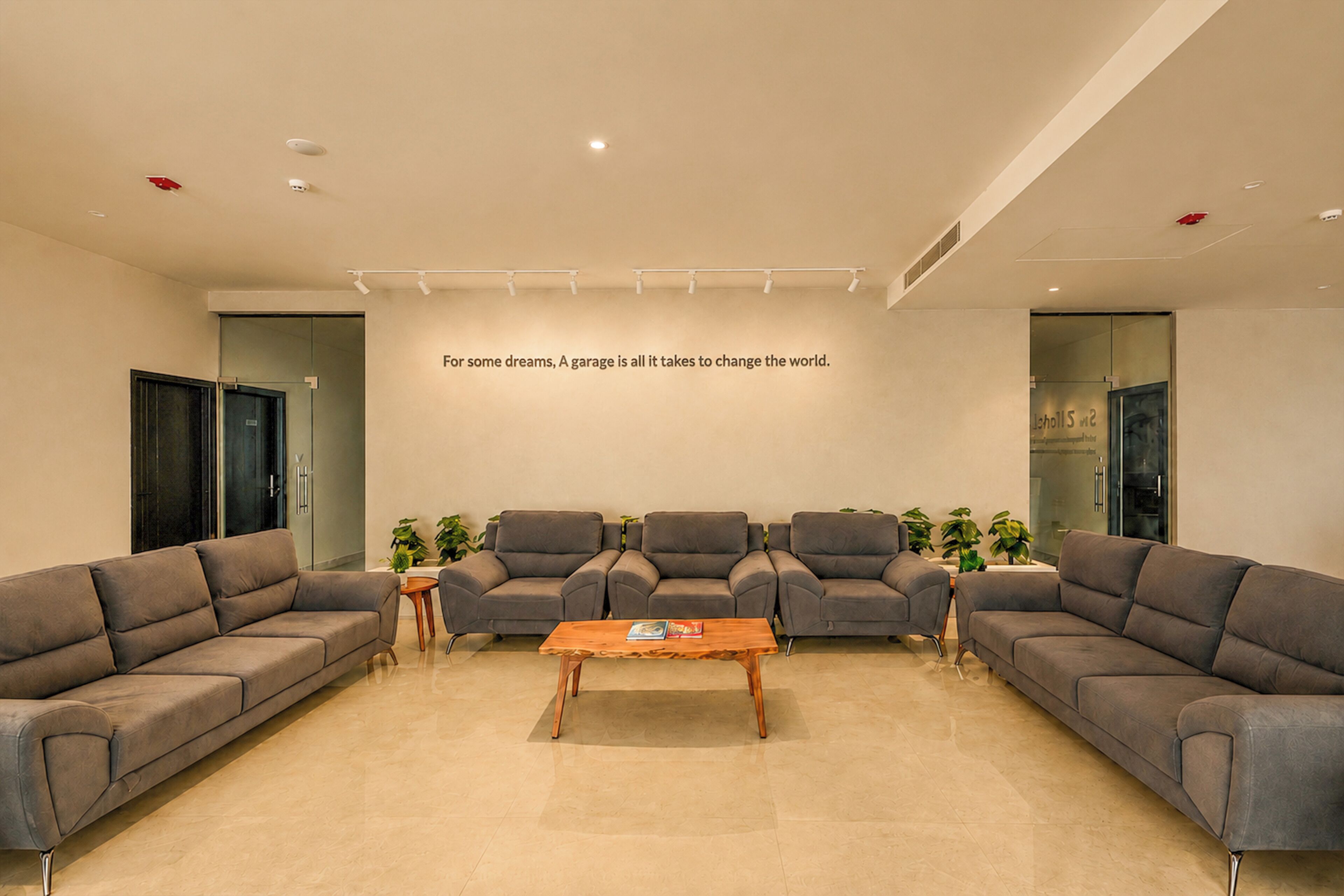 A modern waiting area with a wooden coffee table, grey sofas, and a motivational quote on the wall.