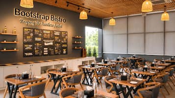 Interior de restaurante con varias mesas y sillas, una pared con menús y lámparas colgantes.