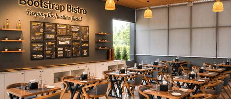 Interior de restaurante con varias mesas y sillas, una pared con menús y lámparas colgantes.