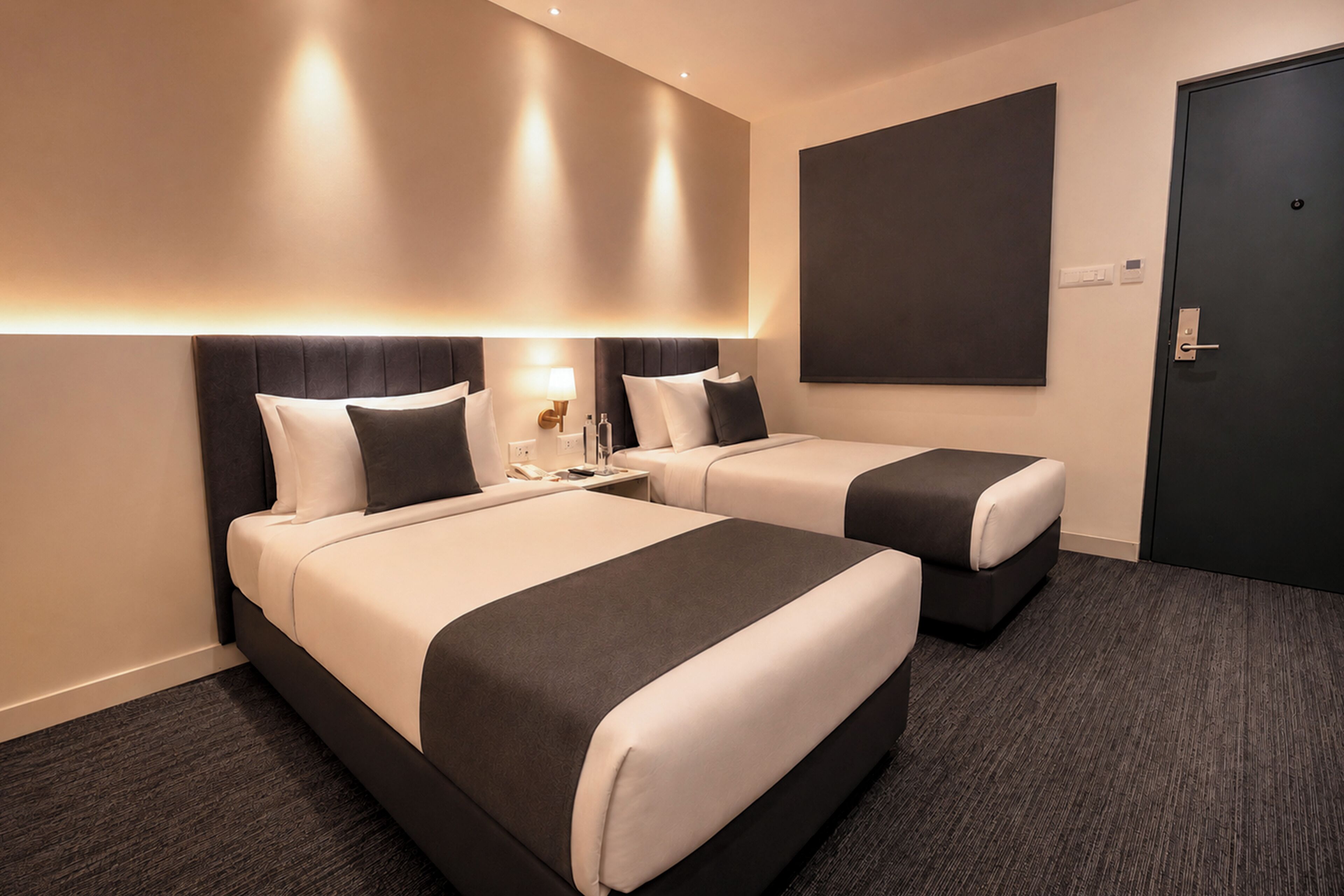 A hotel room with two beds, a dark door, and a large dark artwork on the wall.