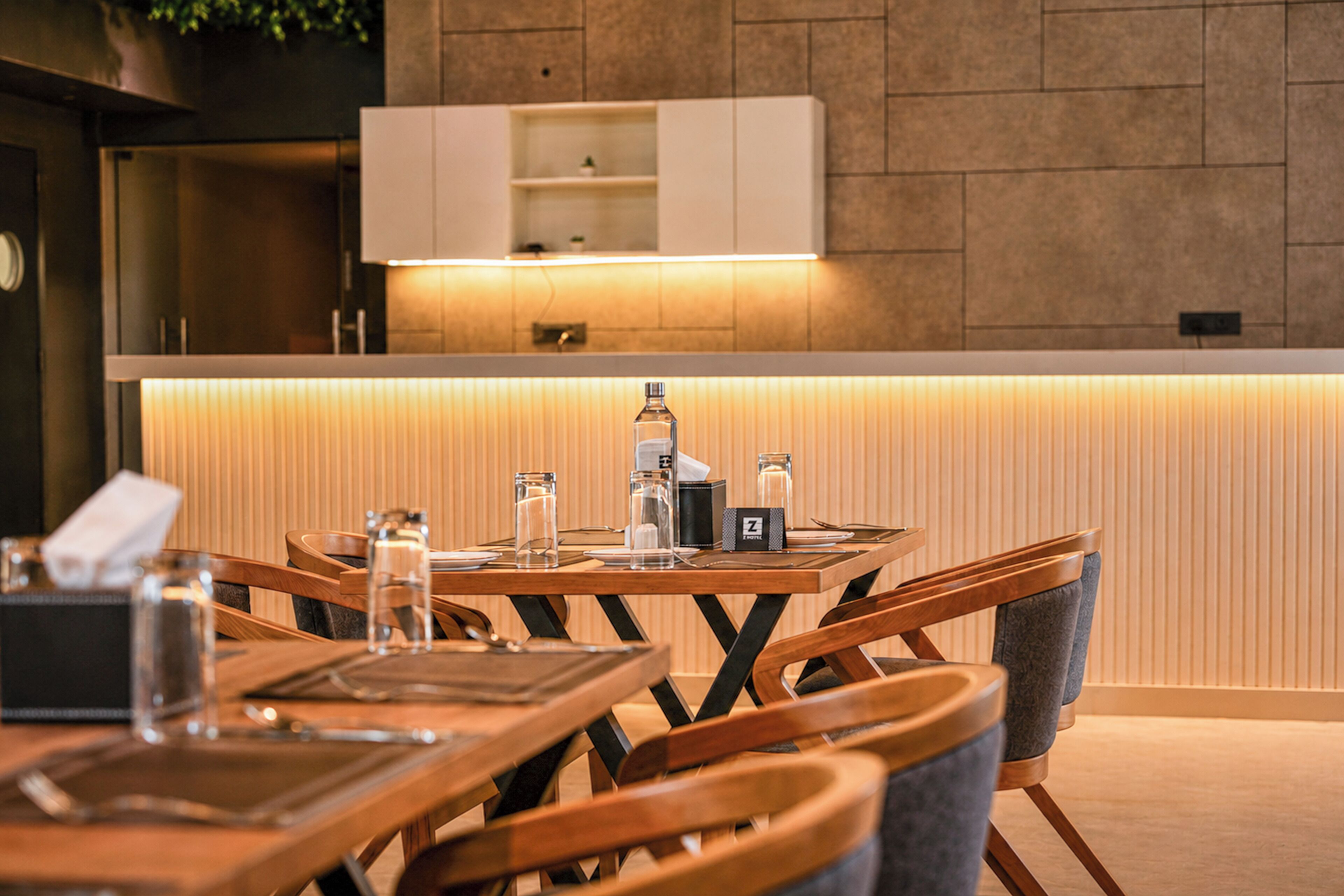 A modern dining area with a wooden table and chairs, a small bar area with a minibar, and a kitchen with a built-in oven and shelf.
