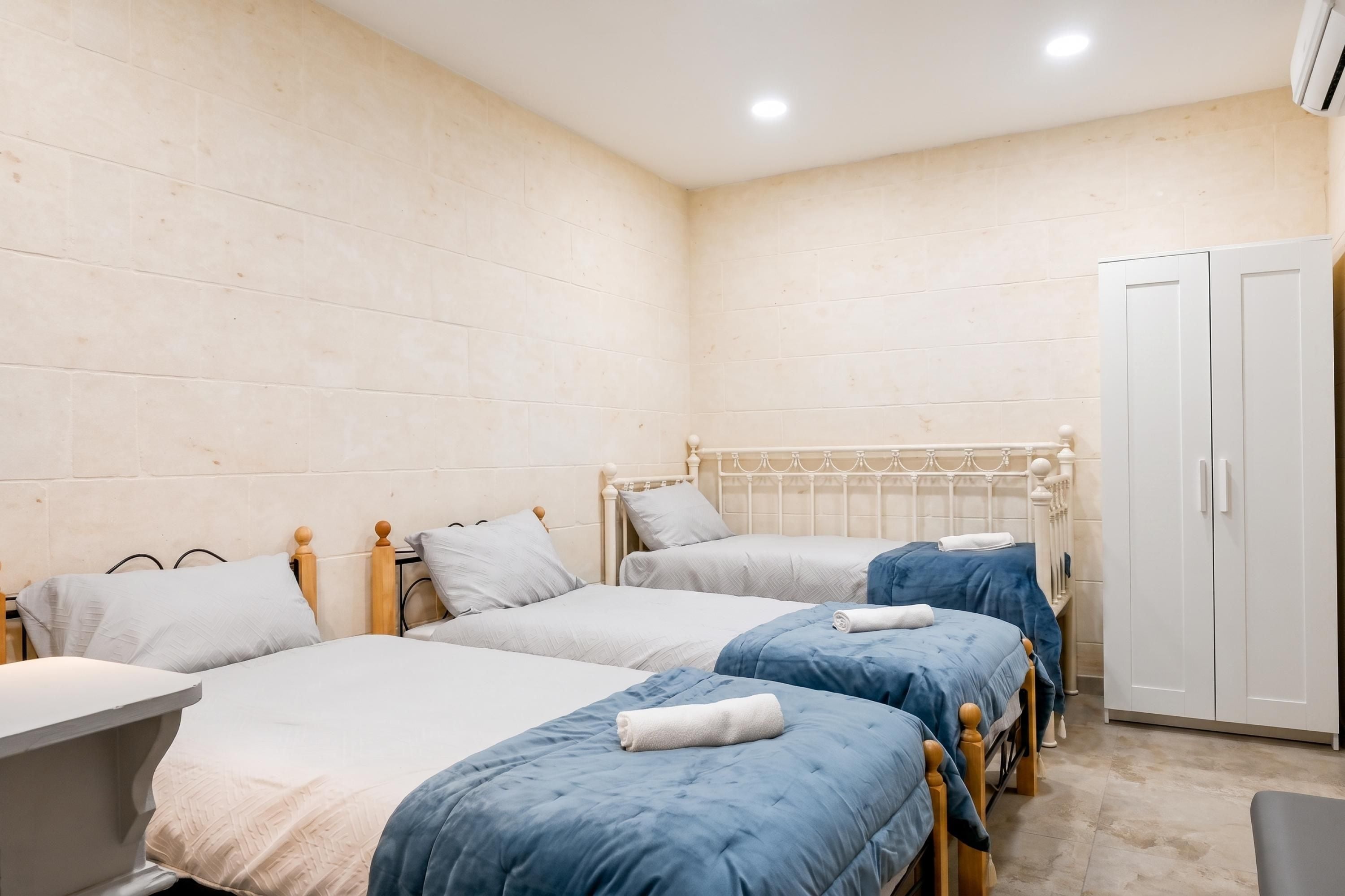 A room with three single beds, a wardrobe, and a small table.