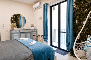 A bedroom with a bed, a dresser, a mirror, a hanging chair, and a balcony with curtains. - Xlendi bay Wonderfull 3 bdr Apart Gozo (Munxar)