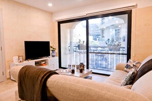 Una sala de estar con televisor de pantalla plana, sofá, mesa de centro y balcón con vistas a la calle.