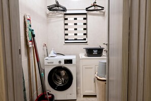 A compact laundry room with a front-loading washing machine, a drying rack, and a small sink. - Xlendi bay Wonderfull 3 bdr Apart Gozo (Munxar)