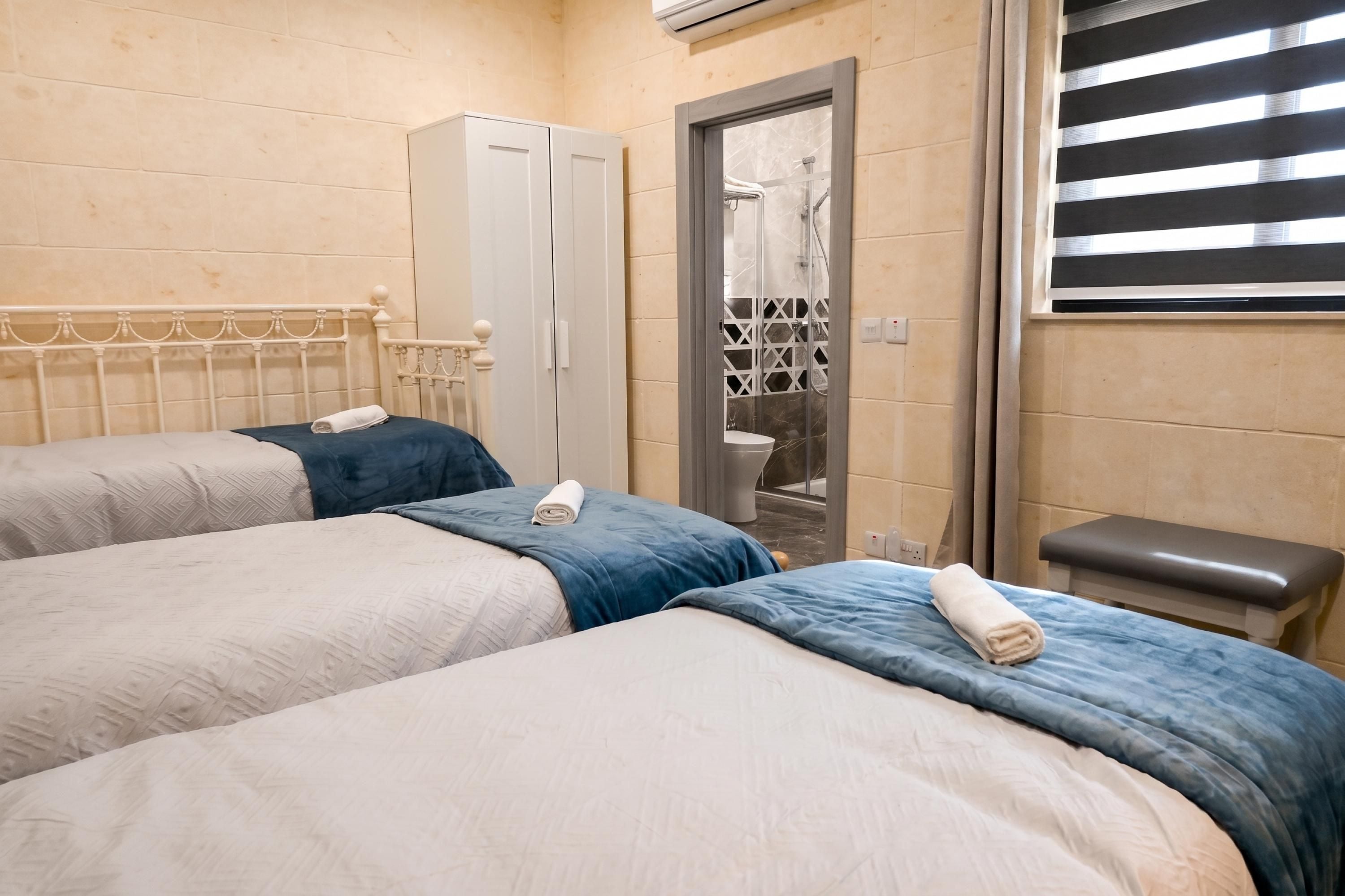 Une chambre d’hôtel avec deux lits, une petite banquette, une armoire et un espace douche.