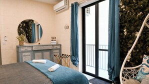 A bedroom with a bed, a dresser, a mirror, a window with curtains, and a balcony with a hanging chair. - Xlendi bay Wonderfull 3 bdr Apart Gozo (Munxar)