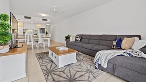 Ein modernes Wohnzimmer mit grauem Sofa, einem Holztisch und einem Essbereich mit weißen Stühlen.