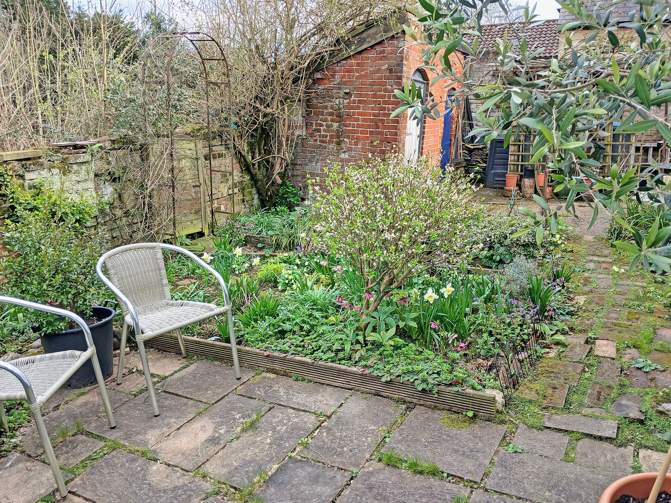 A garden with a brick wall, a metal chair, and a stone pathway.