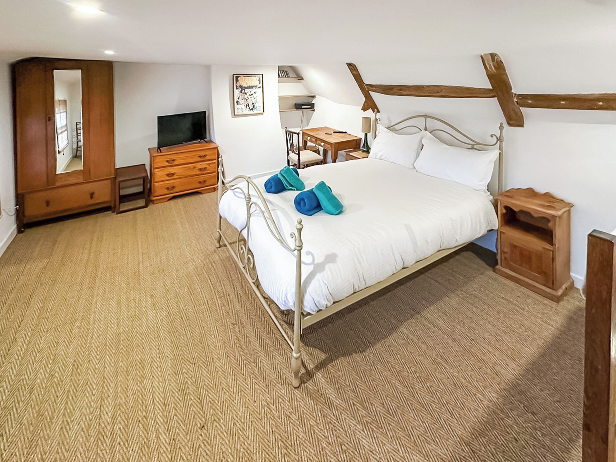 A bedroom with a metal bed frame, a wooden dresser, a television, and a desk with a chair.