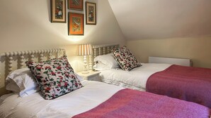 Ein Zimmer mit zwei Betten, jeweils mit weißer Bettwäsche und Kissen mit Blumenmuster, einer Nachttischlampe und gerahmten Bildern an der Wand.