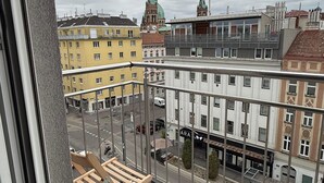 Un balcón con vista a un paisaje urbano, que incluye edificios y una iglesia con cúpula verde.