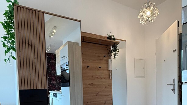 Una habitación moderna con suelo de madera, un banco empotrado con espacio de almacenamiento, una planta colgante y una araña.