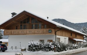 En træchalet med balkon, tag dækket af sne, og et skilt der angiver at det er et skiområde.