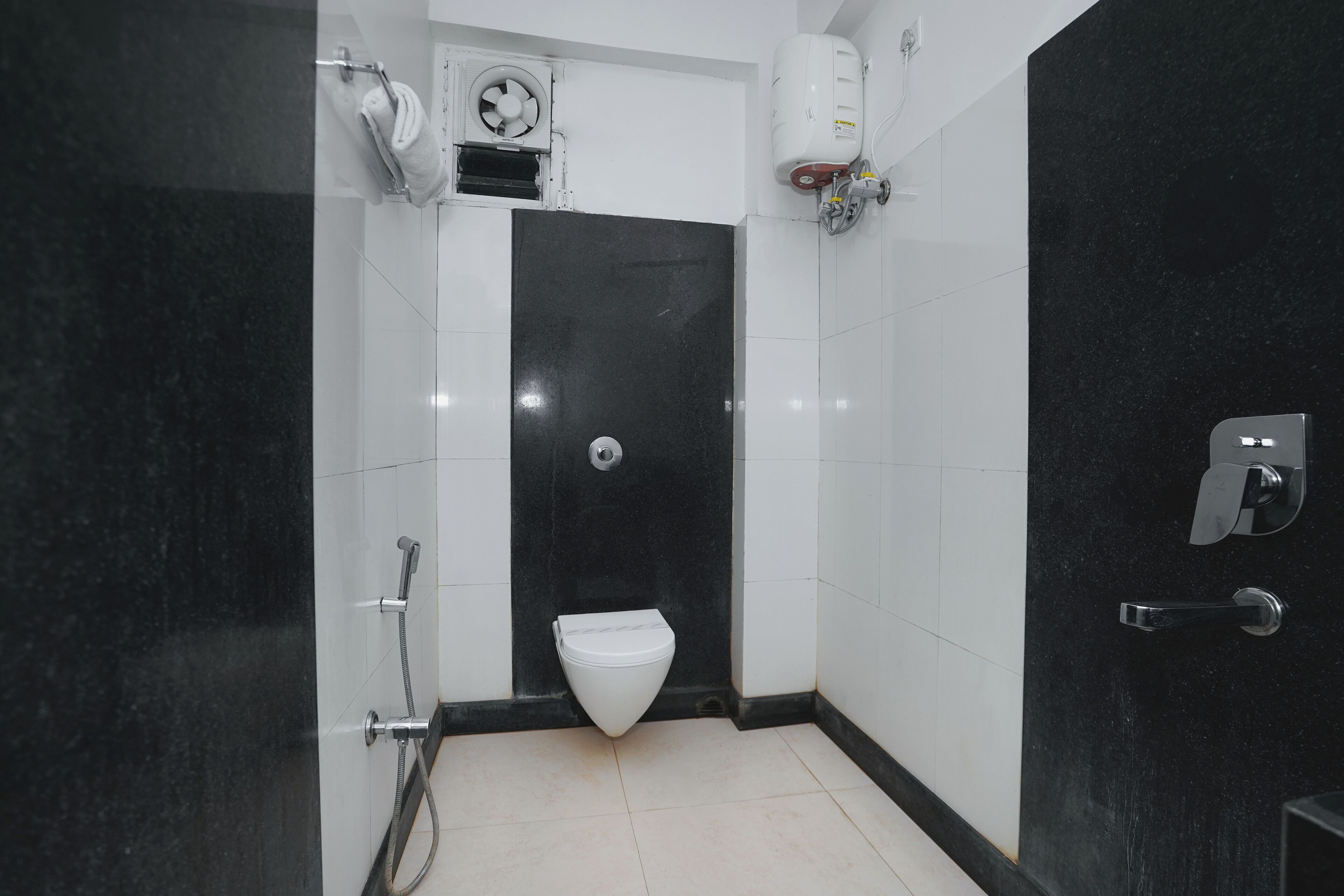 Un baño moderno con diseño de azulejos blanco y negro, un inodoro blanco, zona de ducha y un secador de manos.