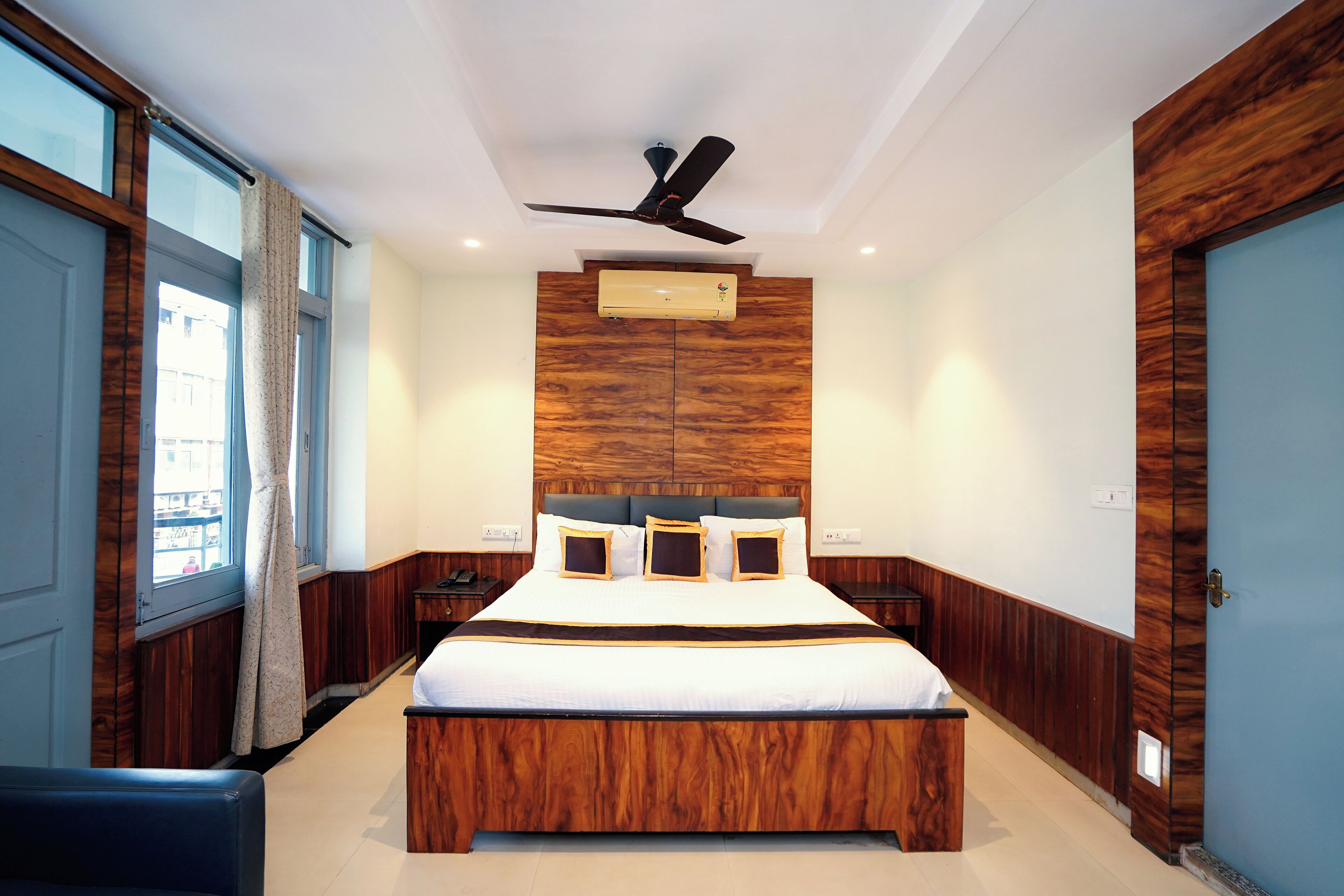 Un dormitorio moderno con una cama grande, paneles de madera, un ventilador de techo y una ventana con cortinas.