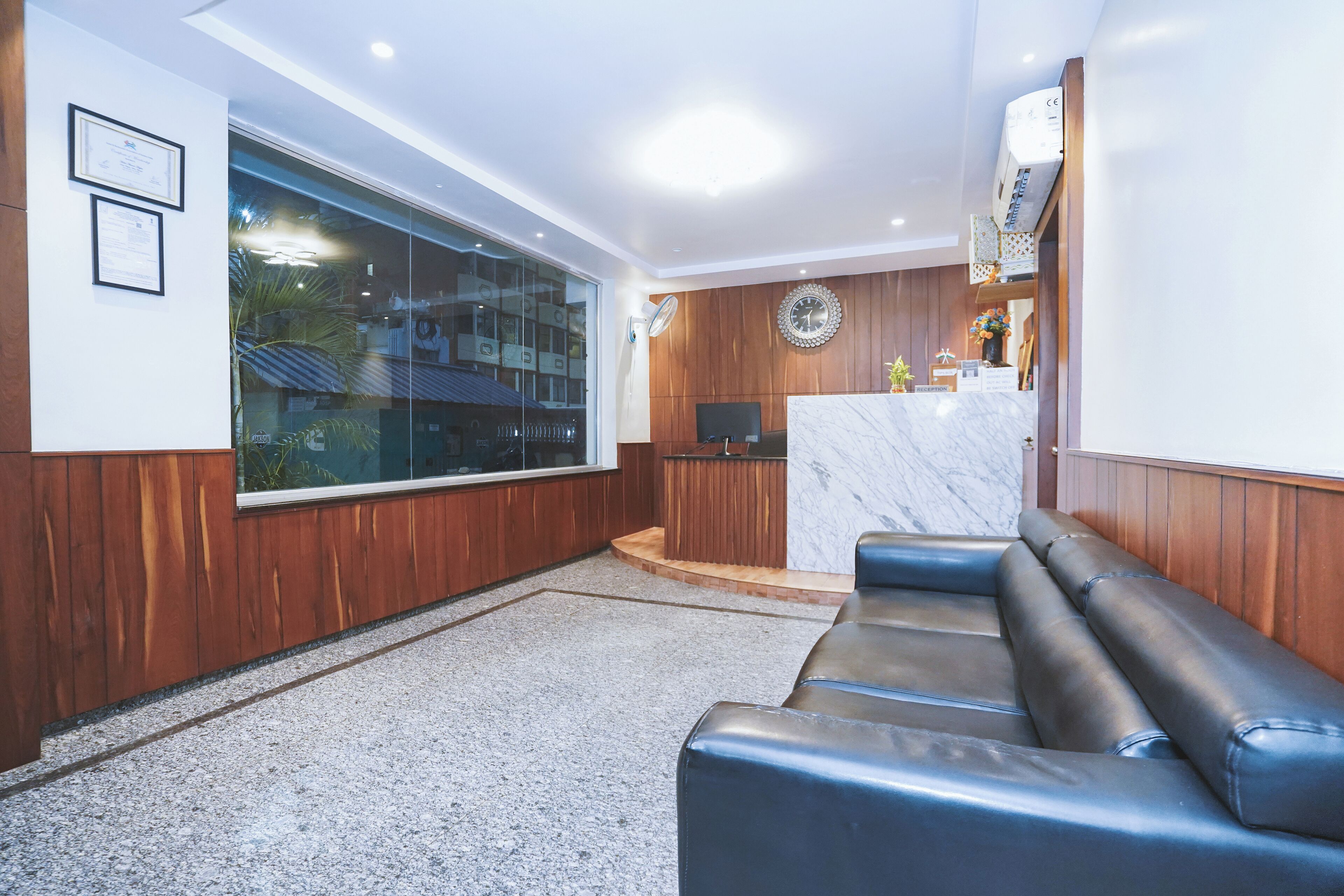 A modern interior with a wooden wall, a large window, a marble reception desk, and a black leather sofa.