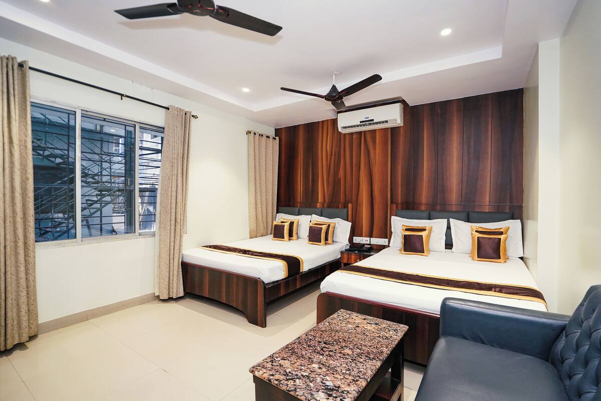 A hotel room with two beds, a ceiling fan, an air conditioning unit, a window with curtains, and a view of the outside.