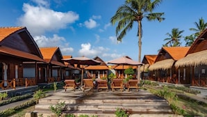 A resort with wooden bungalows, outdoor seating, and a palm tree. - Arjuna Bungalow (Penida Island)