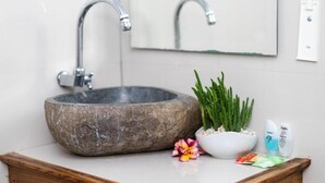 A stone sink with a modern faucet, a mirror, a potted plant, and toiletries on a wooden countertop. - Arjuna Bungalow (Penida Island)