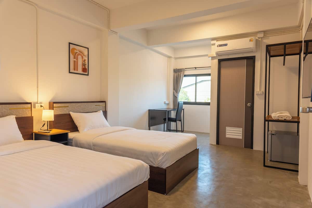 A hotel room with two beds, a desk, a chair, an air conditioning unit, and a wardrobe.