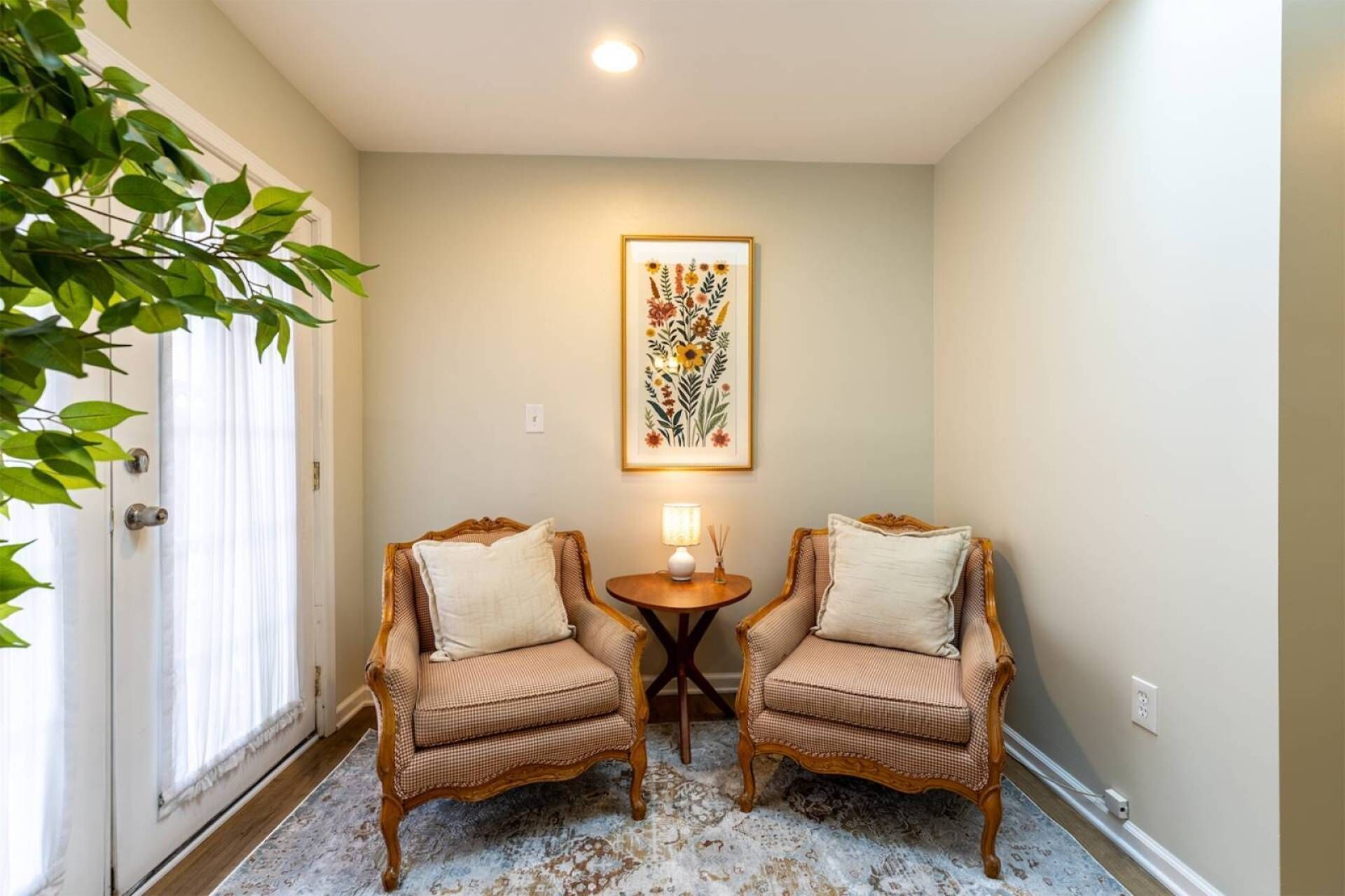 Un pasillo con dos sillones de mimbre, una mesita con lámpara y una obra de arte floral enmarcada en la pared.